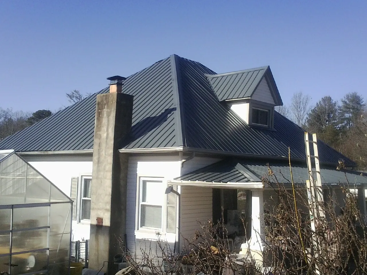 Dark blue standing seam metal roof on a white farmhouse with dormer — Slate & Tile Roof Repair by Roofing Brothers in Kramer