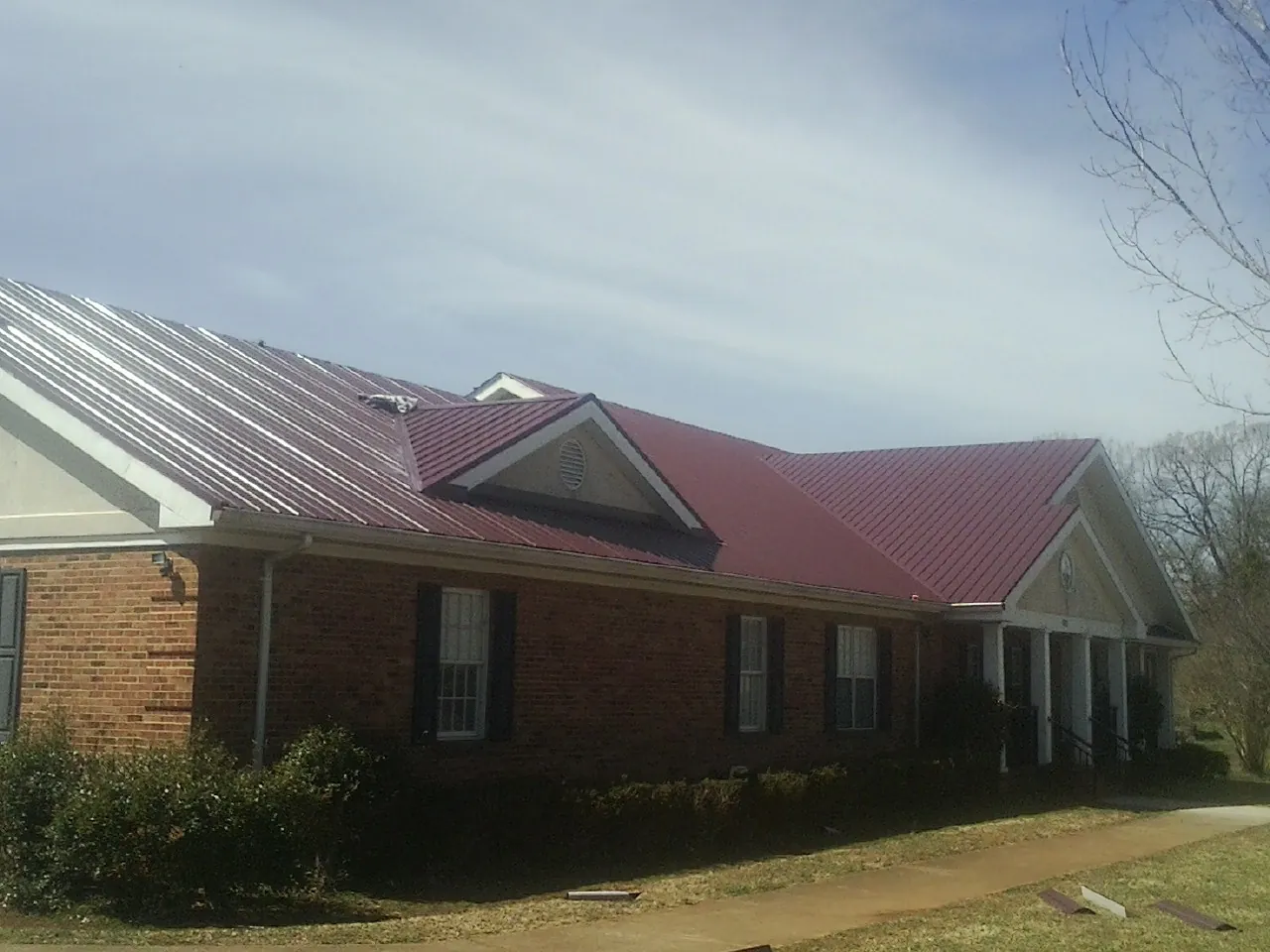Red metal roof with gabled entries on a long brick building, from a Hail Damage Roof Repair job in Kramer