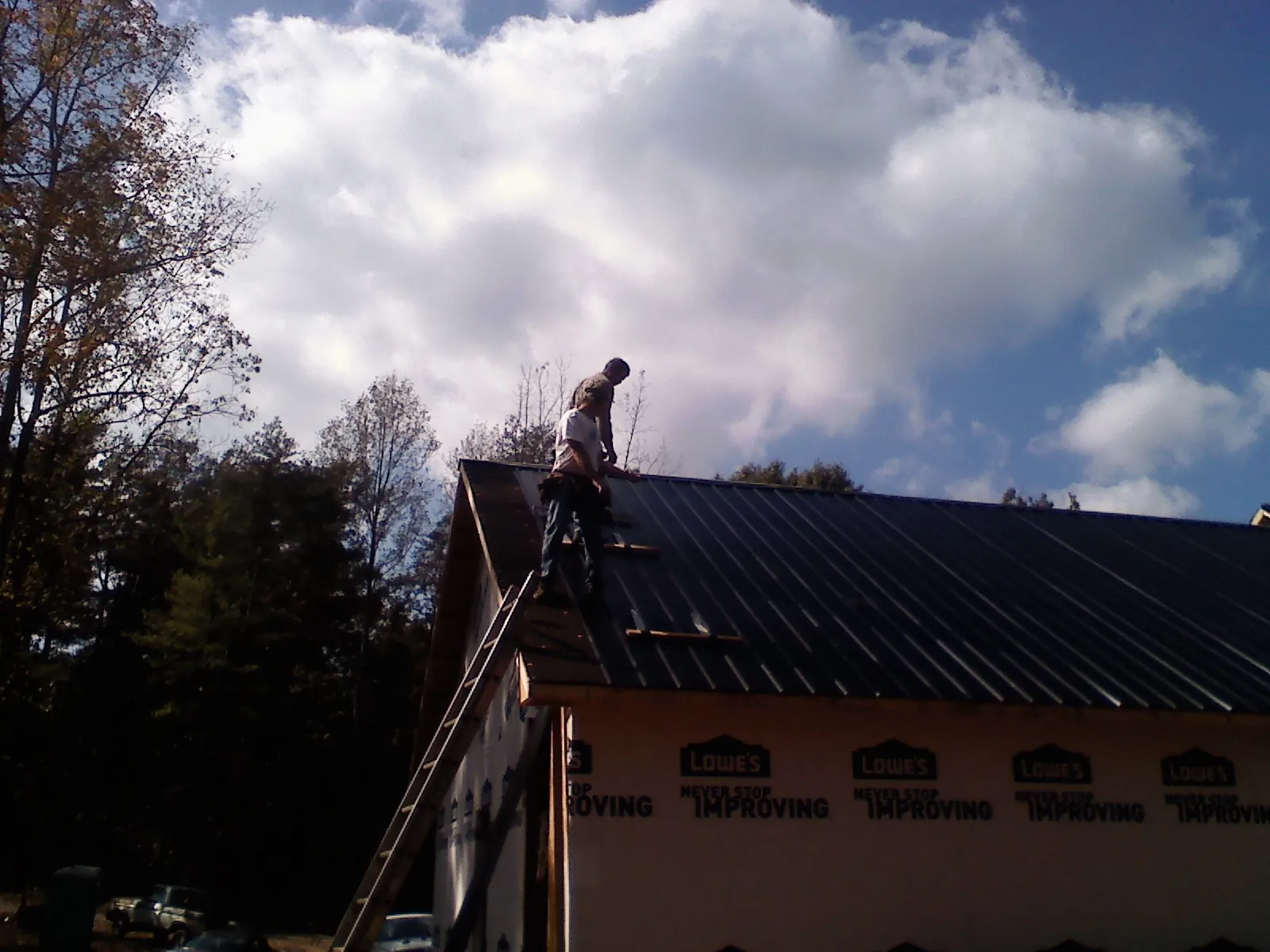 Roofer fastening dark metal panels high against a cloudy sky, from a Roof Inspection job in Kramer